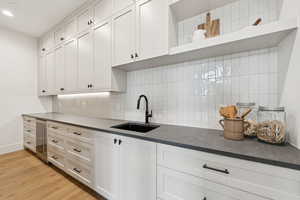 Kitchen featuring open shelves, light wood-style floors, tasteful backsplash, white cabinetry, and beverage cooler