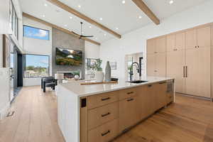 Kitchen featuring light brown cabinets, light wood-type flooring, light stone countertops, a ceiling fan, and a large fireplace
