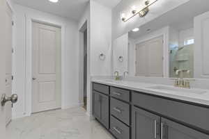 Full bathroom featuring a shower stall, double vanity, light marble finish floors, and a closet
