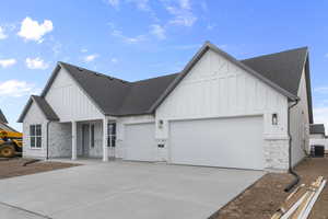 Modern farmhouse with stone siding, an attached garage, board and batten siding, and concrete driveway