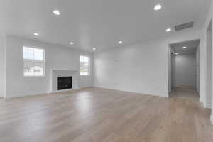 Unfurnished living room featuring a glass covered fireplace, recessed lighting, and light wood-style floors