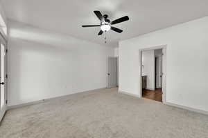 Unfurnished bedroom featuring light colored carpet, ceiling fan, and ensuite bath
