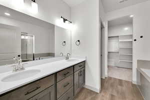 Bathroom featuring a garden tub, double vanity, light wood-type flooring, and a spacious closet
