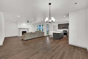 Living room featuring a warm lit fireplace, a chandelier, recessed lighting, dark wood-type flooring, and ceiling fan
