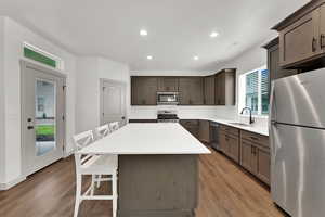 Kitchen with a breakfast bar, appliances with stainless steel finishes, recessed lighting, light wood finished floors, and a center island