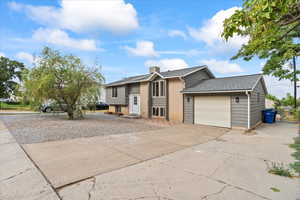 Bi-level home featuring an attached garage, concrete driveway, a shingled roof, and a chimney