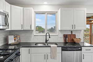 Kitchen featuring dark stone counters, appliances with stainless steel finishes, white cabinets, and healthy amount of natural light