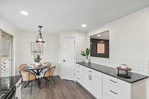 Kitchen with dark stone counters, decorative backsplash, hanging light fixtures, dark wood finished floors, and white cabinetry