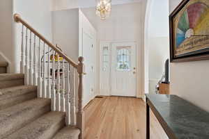 Entrance foyer with light wood-type flooring, stairs, and a chandelier