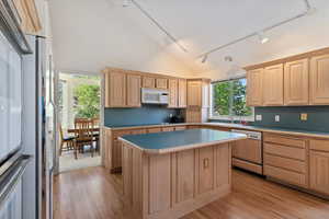 Kitchen featuring track lighting, light brown cabinetry, lofted ceiling, light countertops, and white appliances