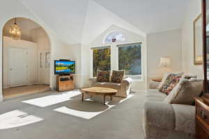 Carpeted living room featuring arched walkways and high vaulted ceiling