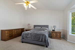 Bedroom featuring light colored carpet, vaulted ceiling, and a ceiling fan