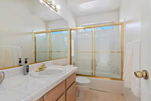 Full bathroom with bath / shower combo with glass door, vanity, and light flooring
