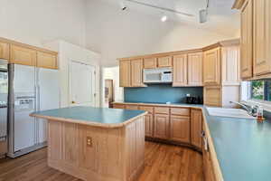 Kitchen with light brown cabinetry, a kitchen island, white appliances, light wood-type flooring, and high vaulted ceiling
