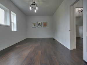 Spare room featuring a chandelier and dark wood-style flooring