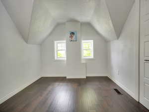 Additional living space featuring a textured ceiling, dark wood finished floors, and lofted ceiling