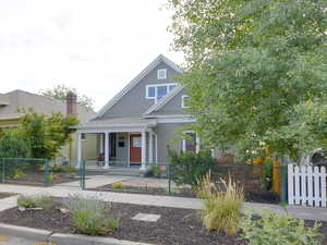 View of front facade featuring covered porch, roof with shingles, and a fenced front yard