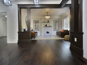 Living room featuring ornate columns, a chandelier, and dark wood-style flooring