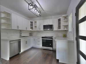 Kitchen with open shelves, glass insert cabinets, appliances with stainless steel finishes, white cabinets, and backsplash