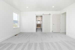 Unfurnished bedroom with a barn door, light colored carpet, connected bathroom, and recessed lighting