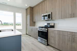 Kitchen featuring stainless steel appliances, modern cabinets, light stone countertops, light wood-style flooring, and recessed lighting