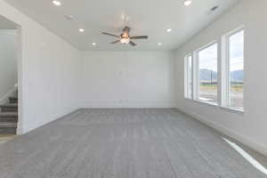 Empty room with a mountain view, stairs, recessed lighting, light colored carpet, and a ceiling fan