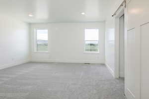 Unfurnished bedroom with a barn door, multiple windows, light carpet, and recessed lighting