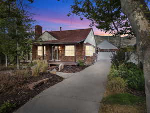 View of front of property with a garage, a chimney, brick siding, covered porch, and an outbuilding