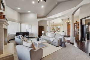 Carpeted living room with arched walkways, high vaulted ceiling, a premium fireplace, a chandelier, and recessed lighting