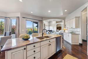 Kitchen featuring open floor plan, light stone countertops, arched walkways, dark wood-style floors, and recessed lighting
