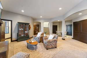 Carpeted living room with arched walkways, recessed lighting, and stairs