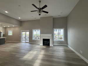 Unfurnished living room featuring a brick fireplace, plenty of natural light, wood finished floors, recessed lighting, and a high ceiling