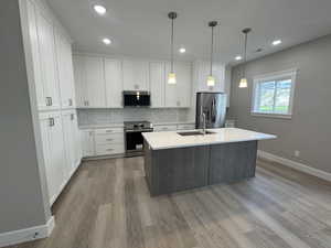 Kitchen with appliances with stainless steel finishes, decorative backsplash, a center island with sink, white cabinetry, and decorative light fixtures