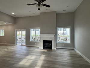 Unfurnished living room featuring a towering ceiling, a fireplace, wood finished floors, recessed lighting, and a ceiling fan
