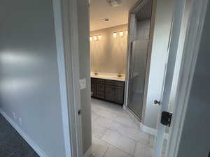 Bathroom featuring double vanity, light marble finish floors, and a shower stall