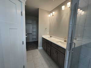 Full bathroom featuring double vanity, light marble finish floors, a stall shower, a textured ceiling, and a spacious closet
