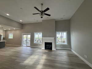 Unfurnished living room featuring a glass covered fireplace, healthy amount of natural light, wood finished floors, recessed lighting, and a high ceiling