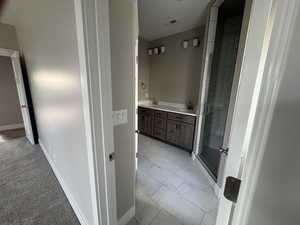 Full bath featuring a shower stall, double vanity, and light marble finish floors