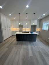Kitchen featuring white cabinetry, a kitchen island with sink, light wood-type flooring, pendant lighting, and recessed lighting