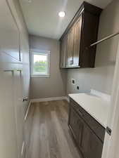 Washroom featuring light wood-type flooring, cabinet space, hookup for a washing machine, and hookup for an electric dryer
