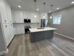 Kitchen featuring decorative backsplash, a kitchen island with sink, appliances with stainless steel finishes, pendant lighting, and white cabinetry