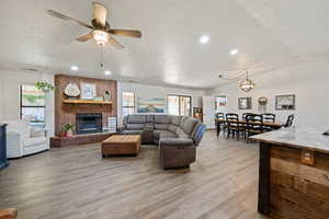Living area featuring a textured ceiling, plenty of natural light, light wood-style flooring, a fireplace, and lofted ceiling