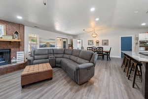 Living room featuring lofted ceiling, a fireplace, light wood-type flooring, recessed lighting, and a textured ceiling
