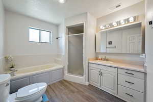 Full bath with a garden tub, vanity, a textured ceiling, dark wood-style floors, and a shower stall