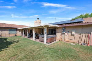 Back of property featuring a hot tub, roof mounted solar panels, a fenced backyard, a chimney, and stucco siding