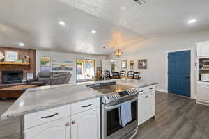 Kitchen featuring stainless steel range with electric stovetop, white cabinets, dark wood-style flooring, a textured ceiling, and vaulted ceiling