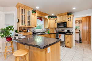 Kitchen with glass insert cabinets, light brown cabinetry, light tile patterned floors, stainless steel electric range, and a peninsula