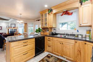 Kitchen featuring a peninsula, open floor plan, light brown cabinetry, dishwasher, and glass insert cabinets