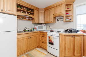 Kitchen with open shelves, white appliances, light brown cabinets, and light countertops