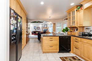 Kitchen featuring open floor plan, black appliances, light brown cabinetry, a peninsula, and light tile patterned floors
